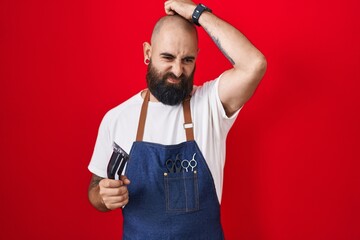 Young hispanic man with beard and tattoos wearing barber apron holding razor confuse and wondering about question. uncertain with doubt, thinking with hand on head. pensive concept.