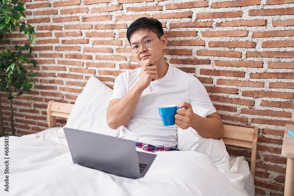 Sticker young asian man drinking coffee sitting on the bed serious face thinking about question with hand on