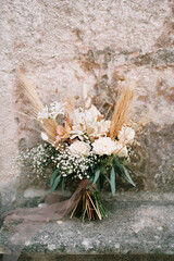 Bride bouquet stands near the wall of an ancient stone building