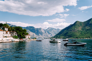 Fototapeta na wymiar Motor boats are moored off the coast of Perast against the backdrop of ancient houses at the foot of the mountains. Montenegro