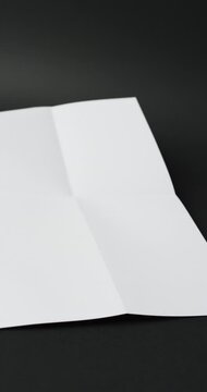 Vertical video of piece of white paper with creases on black background