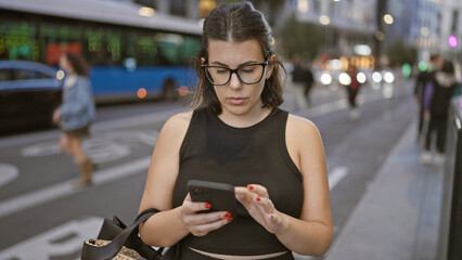 Beautiful brunette hispanic woman in glasses, engrossed in serious smartphone conversation on...