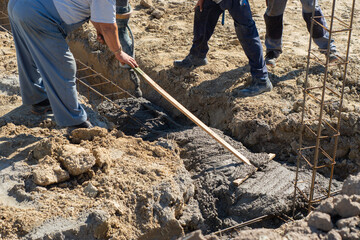 Builders using a concrete to make a foundation footings with steel reinforcement for the new house to build. Concrete pouring to the hole in the ground.