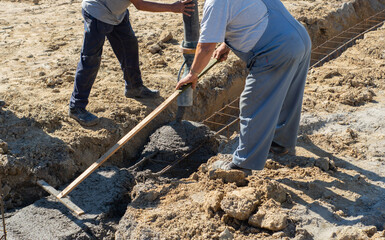 Builders using a concrete to make a foundation footings with steel reinforcement for the new house to build. Concrete pouring to the hole in the ground.