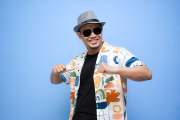 Overjoyed asian man wearing sunglasses dancing, smiles positively, being in high spirit. isolated on blue background. holiday and vacation concept