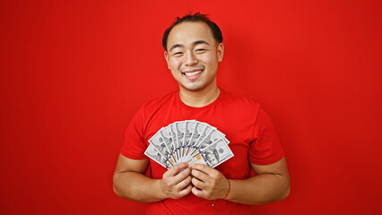 Confident young chinese man, gleaming with happiness, casually holding a heap of us dollars,...