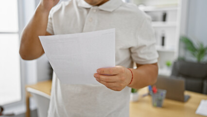 Business professional, man at work in office, holding document while standing indoors. employee...