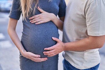 Man and woman couple standing together touching belly at street