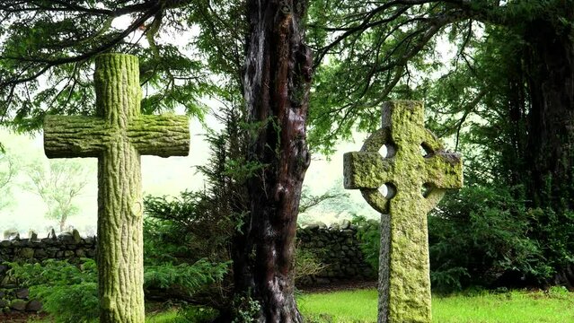 Two old stone crosses under the green trees in summer.