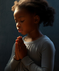 Fototapeta premium Pretty black child girl praying to the Lord - light of god shining down - afro ethnic diversity and religion concept