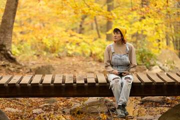 Fototapeta premium Woman with mobile phone and headphones in forest wearing yellow hat, listening to music, taking photos and video call