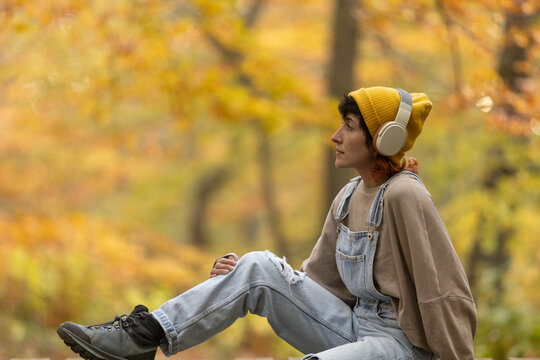 Woman with mobile phone and headphones in forest wearing yellow hat, listening to music, taking photos and video call