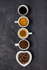 View from above. Some types of coffee in various cups arranged in a vertical row on a black background