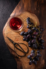 on a rough wooden board, a bunch of black grapes and a pair of scissors and a glass of red wine - 685824286