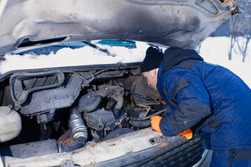 truck breaks down on the road in winter, the driver is repairing the car in winter clothes. working...