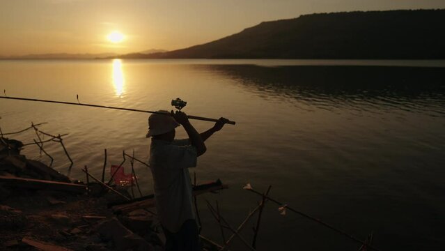 Fishermen are using fishing rods relaxation outside in the lake during Silhouette sunset.