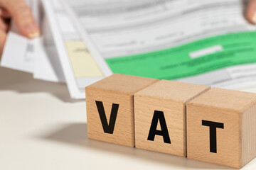 VAT settlement in Poland, abbreviation for value added tax, tax on goods and services paid by sellers and buyers, finance concept, written on wooden blocks and stack of held documents, bureaucracy - obrazy, fototapety, plakaty