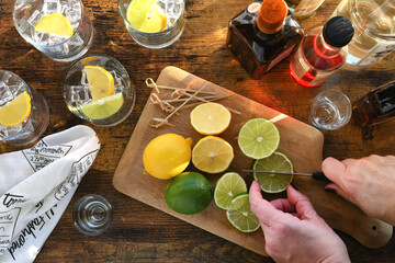Female preparing cocktails with liquor alcohol lemons limes on a wooden bar - high angle overhead...