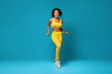 Fototapeta na wymiar Happy black woman in sportswear measuring waist with tape, studio