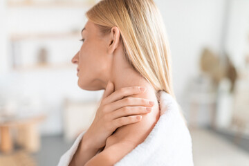 young blonde woman touching and self massaging neck in bathroom