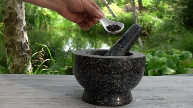 The hand is putting the black pepper in the grey stone mortar in slow motion