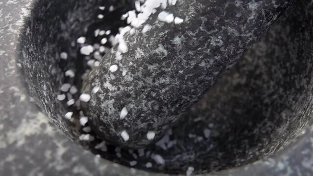 Close-up of a white sea salt falling on the pestle in the grey stone mortar