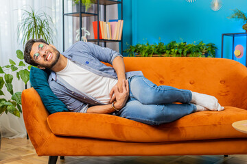 Indian young man lying on sofa feeling sudden strong abdominal stomach ache gastritis problem....