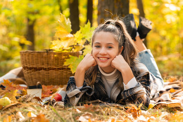 A young girl in the autumn forest is sitting on a plaid plaid and is enjoying the peace and sunshine, the beautiful atmosphere of autumn