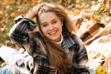 A young girl in the autumn forest is sitting on a plaid plaid and is enjoying the peace and sunshine, the beautiful atmosphere of autumn