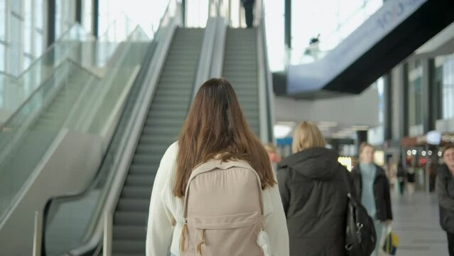 Unrecognizable caucasian woman traveler with backpack walking on escalator in international airport. time to Travel, Vacation, trip and Transport concept 4K