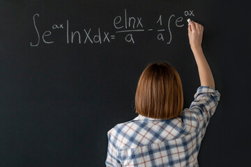 A young female student writes a complex mathematical formula on the blackboard