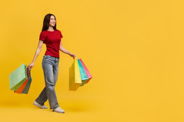 Happy asian lady in casual outfit walking with shopping bags
