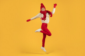 Fototapeta na wymiar lady in winter clothes leaping with joy on yellow backdrop