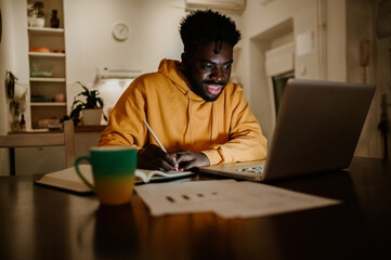 A focused african american man is following an online course on a laptop while sitting at home late...