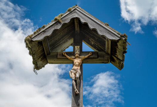 Wooden christian wayside cross with jesus christ figurine against blue sky with clouds