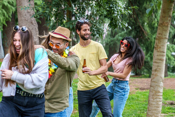 Vibrant group of friends, including Asian man, dancing and laughing with beers in park.