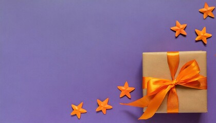 banner flat lay of brown gift box with a orange satin ribbon bow and stars shapes on vibrant purple background at the bottom on the right with copy space holiday autumn and halloween concept