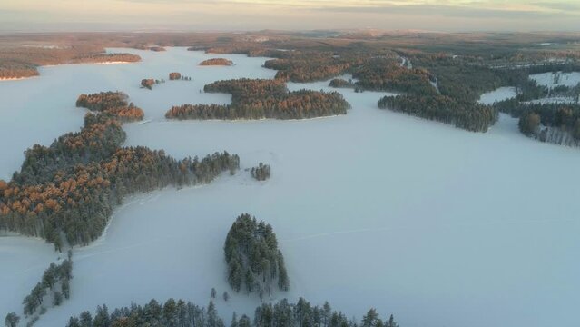 Winter in Finland; slow drone flight over a snow covered landscape with boreal forests and frozen lakes in southern Lapland at sunrise