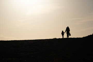 Silhouette d'une femme tenant un enfant par la main, se promenant au soleil couchant	
