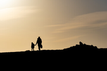 Fototapeta premium Silhouette d'une femme tenant un enfant par la main, se promenant au soleil couchant 