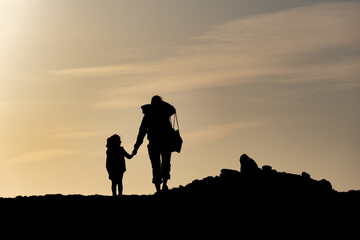 Obraz na płótnie Canvas Silhouette d'une femme tenant un enfant par la main, se promenant au soleil couchant