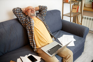 Side view of displeased frustrated aged man procrastinating to finish project sitting on couch with...