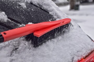 Cleaning the car snow with a red brush. 