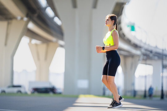 Gorgeous European girl runs under an overpass during a morning workout in the park. Beautiful spanish young woman standing in sport clothes at weekend during morning training. Sport, health, cardio.