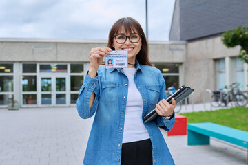 Female teacher showing ID card badge, outdoor educational building