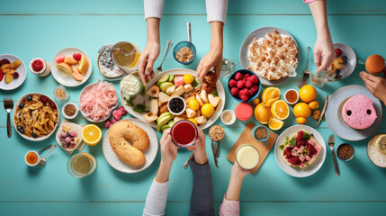 Breakfast spread with hands reaching for various dishes, including eggs, bacon, pancakes, fruits, and beverages on a colorful wooden table.