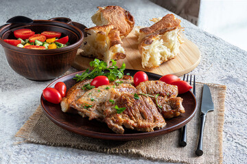 Pork chops, vegetable salad and freshly baked bread. Serving in rustic style, ceramic dishes. Two-course lunch. Hot meat dish. Healthy food, delicious homemade food