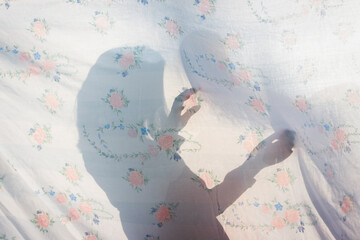 Sombra y forma de una niña pequeña a través de una sábana translúcida en una tarde de...
