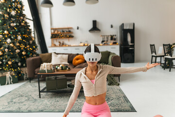 Engrossed in yoga practice, a fitness enthusiast wears virtual reality goggles by a Christmas tree.