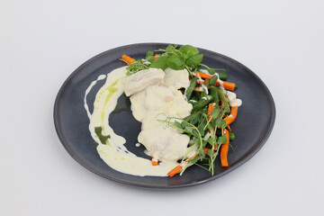 Turkey fillet in white sauce with vegetables on a dark plate on a white background